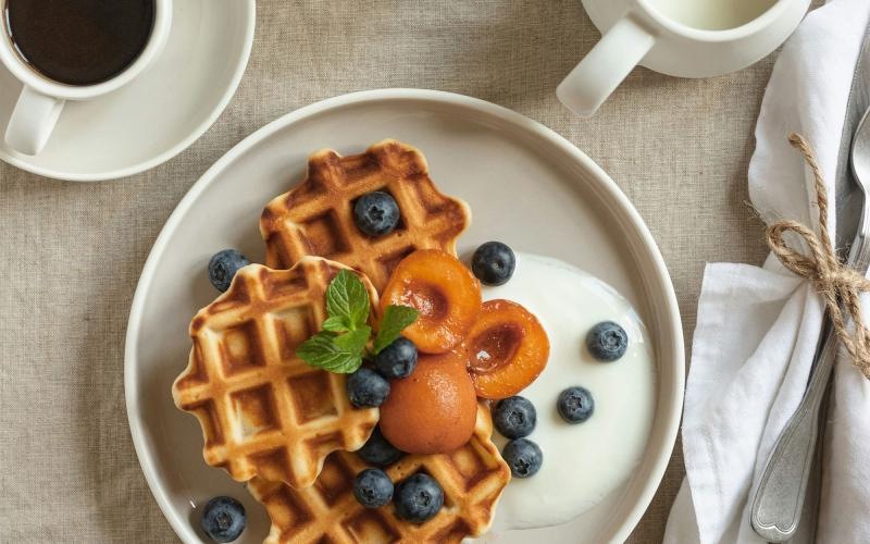 a plate of blueberries and waffles and a cup of coffee